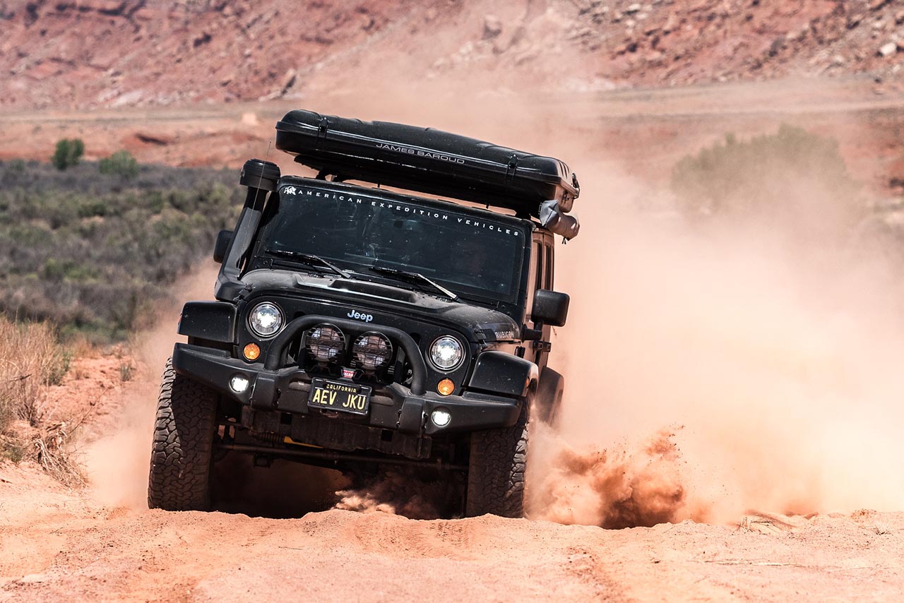 AEV Jeep with snorkel, kicking up a large amount of dust while overcoming an obstacle.