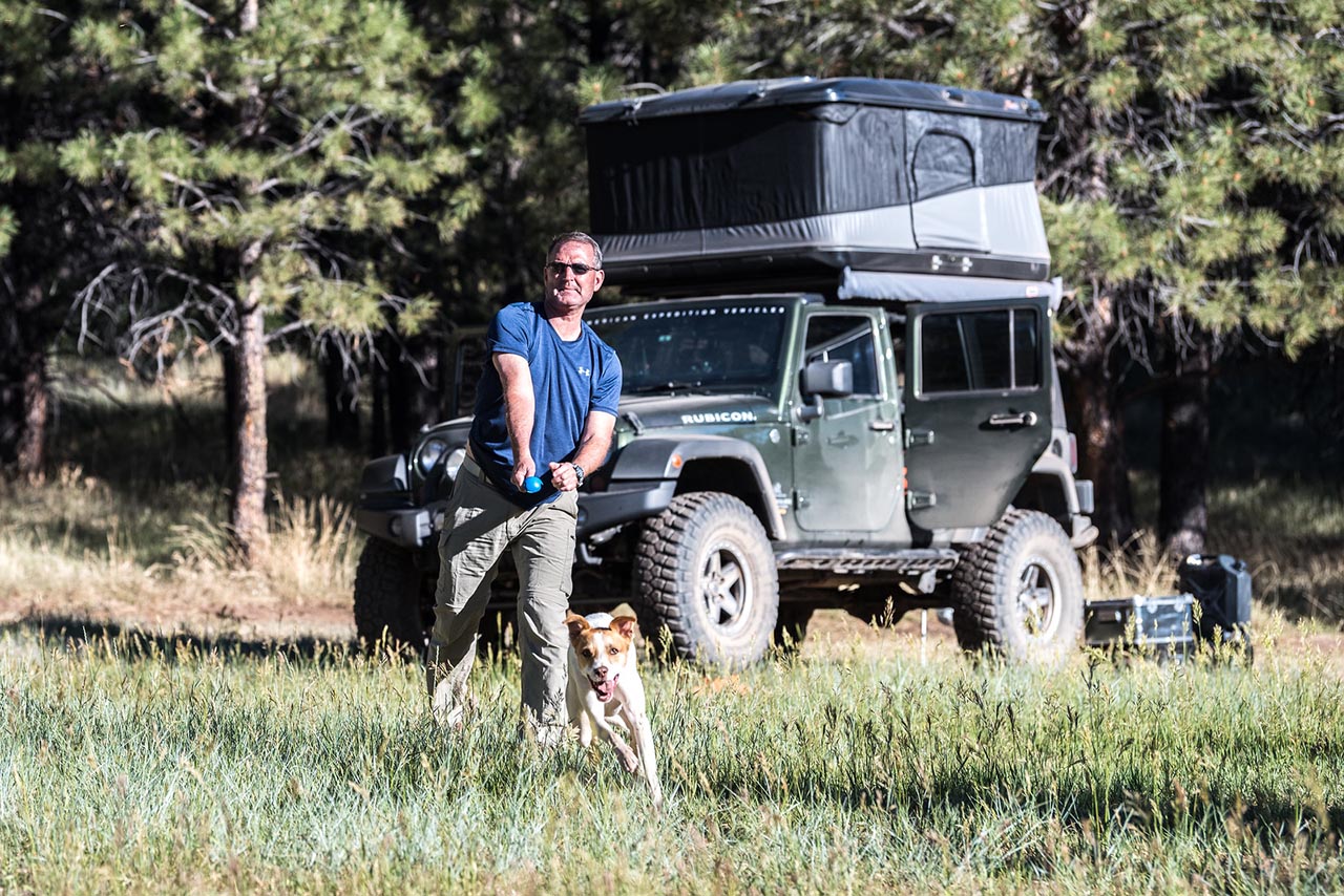 Tour member playing fetch with his dog in front of a Jeep.